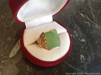 Ring displayed in open red velvet ring box on marble surface, three-quarter view of jade and band