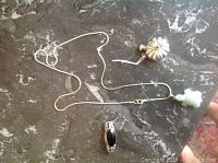 Sterling silver chain with jade turtle pendant, black stone brooch, and silver perfume bottle shown on marble surface.