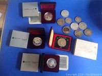 Five commemorative silver dollars in RCM presentation boxes alongside loose coins