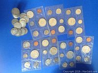 Assortment of loose half-dollars and multiple sealed mint sets on blue background