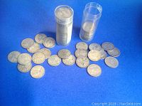 Two plastic coin tubes filled with rolled quarters and loose quarters spread on blue background