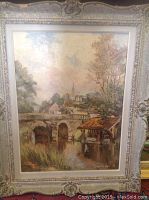 Full view of framed oil painting showing rural bridge and village scene