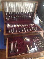 Wooden hinged box open showing upper tray with knives in slots and middle tray with forks and spoons in burgundy velvet holders