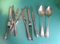 Overview of 2 spoons and 6 knives on turquoise background