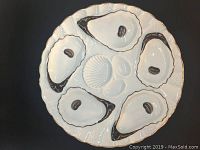 Top view of a single white porcelain oyster plate showing six molded wells and gilt edging