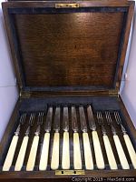 Open wooden presentation case with gray felt lining showing six fruit knives and six fruit forks with ivory-colored handles