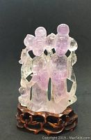 Front view of amethyst figural carving on wooden base against black background