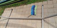 Photo showing metal frame base for the hammock on a paved surface with a striped nylon hammock folded on the side.