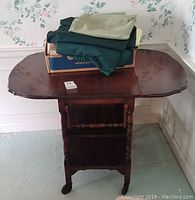 Top and side view of dark wood vintage rolling tea cart with drop leaf sides, scalloped edges, and items placed on top.