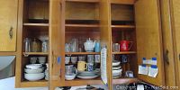 Kitchen cabinet with stacked plates, coffee cups, glassware including glasses and wine glasses