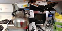 Oster microwave oven on countertop with stainless steel tea kettle in front and yellow-topped ceramic canister and white patterned baking dishes behind.