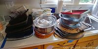 Assorted bakeware items including multiple Pyrex glass baking dishes, mixing bowls, cake pans, and pie plates arranged on kitchen counter.