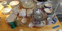 Wide view of the entire lot showing graduated stacks of plates, bowls, a cut glass pitcher, tureens with lids and ladles, various serving bowls and platters, salt and pepper shakers, muffin pan and other kitchen items.