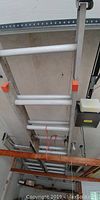 Photo of the two aluminum extension ladders stored mounted on the rafters in the garage, showing their length and condition.