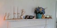 Wide view showing all items arranged on a mantel including miniature ship models, ceramic figurines, candlesticks, clock, barometers, and blue vase with flowers