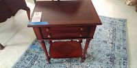 End table with two drawers, fluted legs, brass knobs, and diamond patterned lower shelf on pale Safavieh area rug.