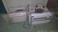 Photo showing three window air conditioners and one small heater, arranged on a floor with power cord visible
