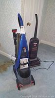 Photo showing front view of blue Bissell ProHeat carpet cleaner and black Hoover upright vacuum