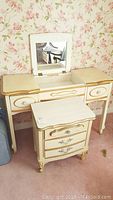 Vintage cream-colored vanity with gold trim, flip-up mirror, three drawers, showing scratches and stains
