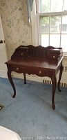 Full view of classic dark wood Bombay Company desk with curved legs in room with floral wallpaper and blue carpet