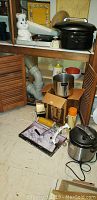 Photo shows shelf with Pillsbury Doughboy cookie jar, Oster Roaster oven, and items stored below including a metal pot, cardboard box, and electric appliances.