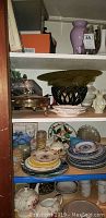 Shelf with stacks of assorted plates, bowls, and decorative pottery including dishes described such as Currier and Ives plates and maple leaf dish.