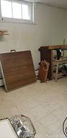 Wide view of router table mounted on wood frame, folding tables and dollies against wall