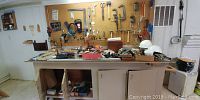 Wide view of pegboard with various hand tools hanging and workbench with assorted tools, boxes, and items laid on it.