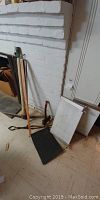 Photo showing two long metal axes leaning against a white brick wall on a basement floor, along with a black rubber door mat and other items.