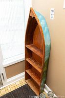 Full view of hand-painted wooden shelf shaped like a boat, showing ocean scene on exterior with three interior shelves, standing in a corner.