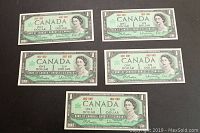 Five uncirculated 1967 Canadian Centennial one dollar bills front side laid out in two rows on a dark surface.