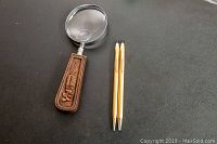 Two vintage Cross pens and a magnifier with a wooden handle on black surface, showing overall items.