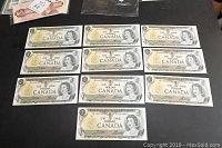 Ten uncirculated Canadian one dollar bills arranged on a flat surface showing front side with Queen Elizabeth II, serial numbers, and official signatures.