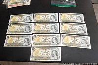 Ten uncirculated Canadian one dollar bills laid out flat showing front sides with portrait of Queen Elizabeth II and serial numbers
