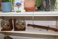 Photo showing two vintage armillary sphere bookends on wooden L-shaped bases and a long wooden serving set with metal hinges on a stand all placed on a shelf