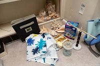 Blood pressure monitor box, handmade soaps box, assorted seashell jars, coral piece, fabric with blue floral design, and candle holder on carpet.