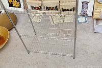 Full view of metal shelving stand showing wire mesh shelves and tubular metal legs.