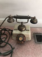 Vintage rotary dial telephone with brass and cream body, rotary dial, and fabric-covered cord on carpeted surface