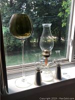 Three oil lamps on a windowsill including one tall amber glass lamp, one large clear glass lamp, and two small matching lamps with metal bases.