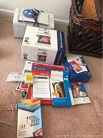 Photo showing Sony Picture Station DPP-FP55 printer box, Samsung ML-2165 printer on top with cables, and multiple printer paper and ink cartridge boxes arranged on carpet.