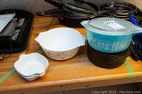 Overview of lot showing multiple bowls and dishes on a wooden surface, including the turquoise Pyrex dish with lid and white CorningWare bowl and dish