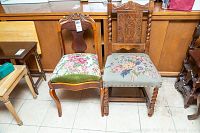 Two vintage wooden chairs side by side on tiled floor, showing carved wood details and floral upholstered seats