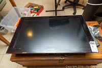 Samsung 31" flat-screen TV lying face up on a wooden chest, reflecting overhead light.