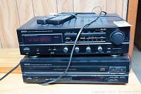 Front view of Denon AM/FM stereo receiver DRA-545R stacked on Denon 5-disc CD changer DCM-340 including remote controls on top.