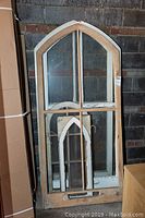 Large wooden window frame with smaller nested arched frame inside, showing paint wear and intact glass panes