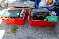Two red bins with camping gear including a black Coleman skillet, green Coleman stove, propane tanks, and white plates.