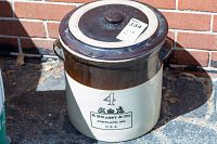 Vintage E. Swasey & Co. stoneware crock pot, size 4, with lid, on outdoor stone surface against brick wall background.