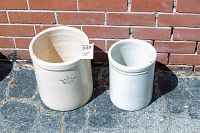 Pair of two stoneware crock pots outside on stone surface against brick wall, one larger marked with blue crown and '2 USA', other smaller and plain white.