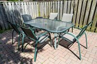 Full view of garden table with glass top and six chairs around it on a paved patio.