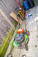 full side view of walk-behind mower showing green deck, orange fuel tank and black engine housing